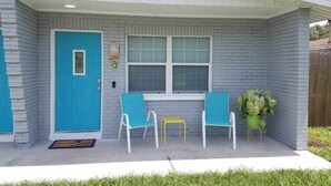Ein Haus mit blauer Tür, zwei Stühlen, einem kleinen Tisch und einem Blumentopf.