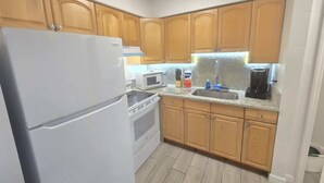 Eine Küche mit Holzausstattung, einem weißen Kühlschrank, einer Mikrowelle, einem Backofen, einer Spüle und einer Kaffeemaschine.