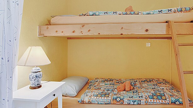 Ein Stockbett mit gemustertem Bettbezug, ein Nachttisch mit Lampe und ein Kopfkissen.