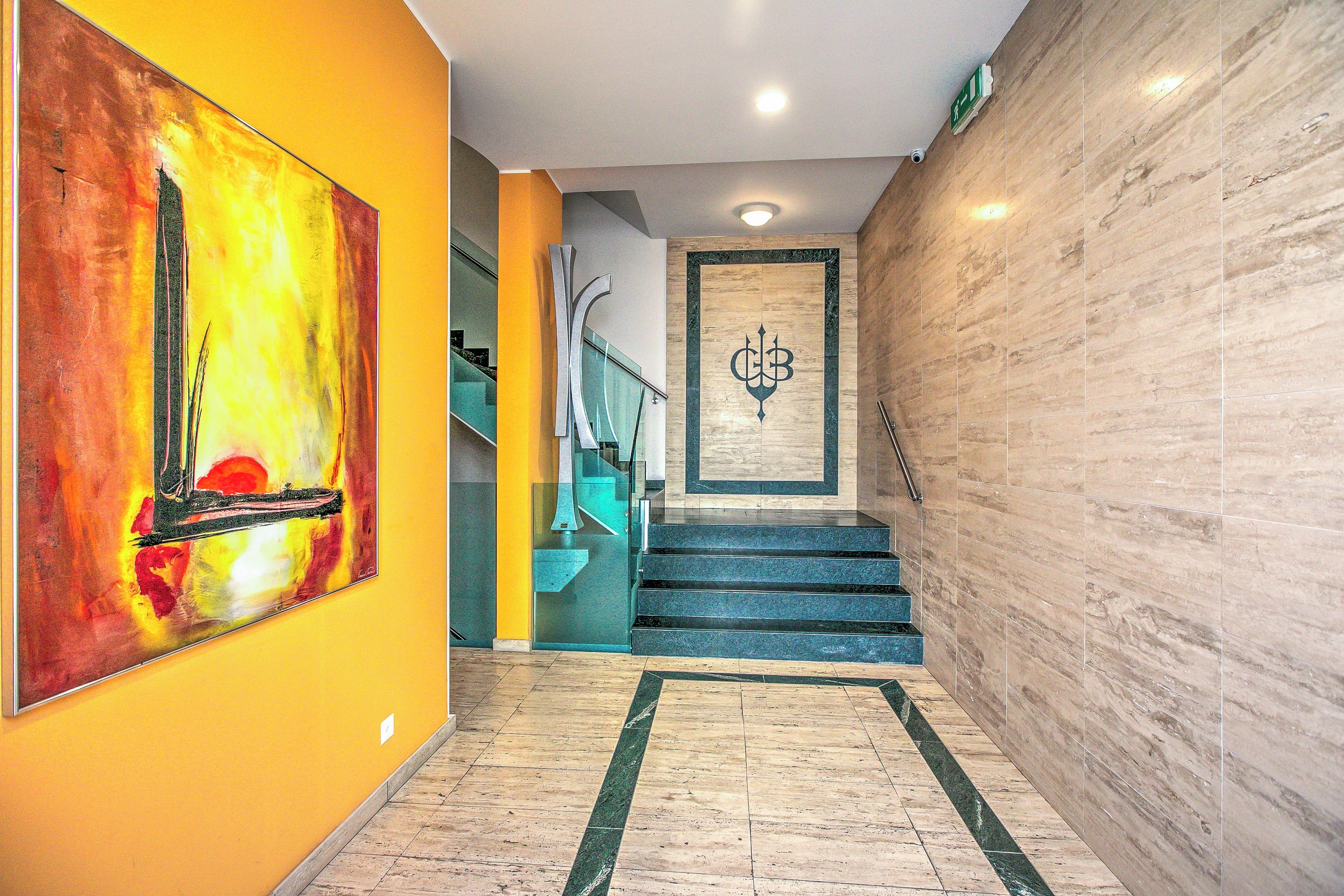A modern interior with a staircase, a large abstract painting, and a marble wall.