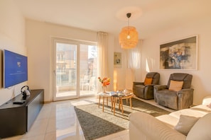 Una sala de estar con televisor, sofá, sillones y una mesa con libros.