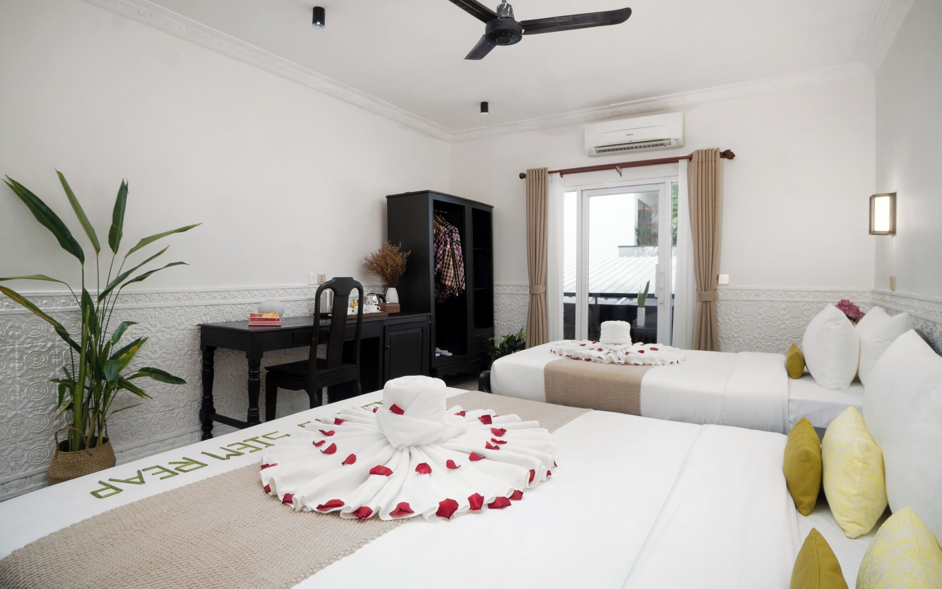 Una habitación de hotel con cama, escritorio, armario, planta en maceta y ventilador de techo.