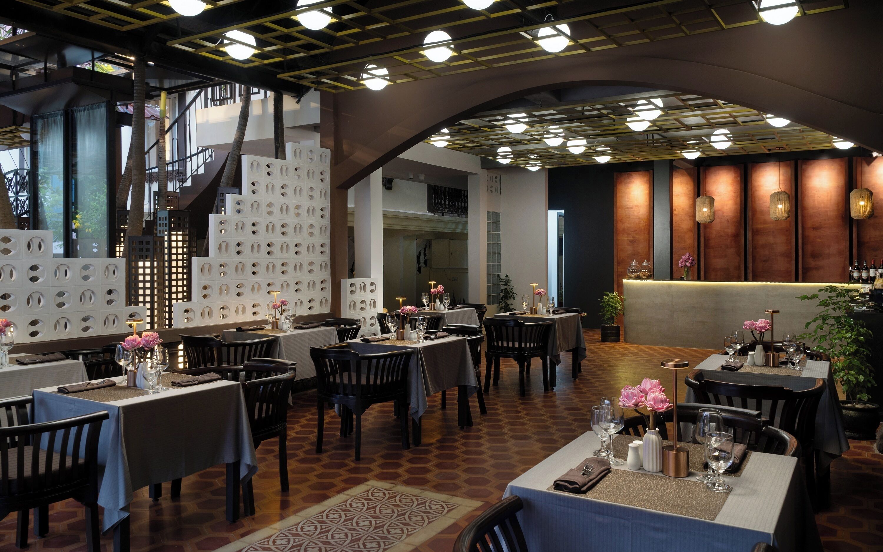 L’intérieur d’un restaurant, avec des tables dressées pour le service, un coin bar et un élément de décoration servant de séparation.