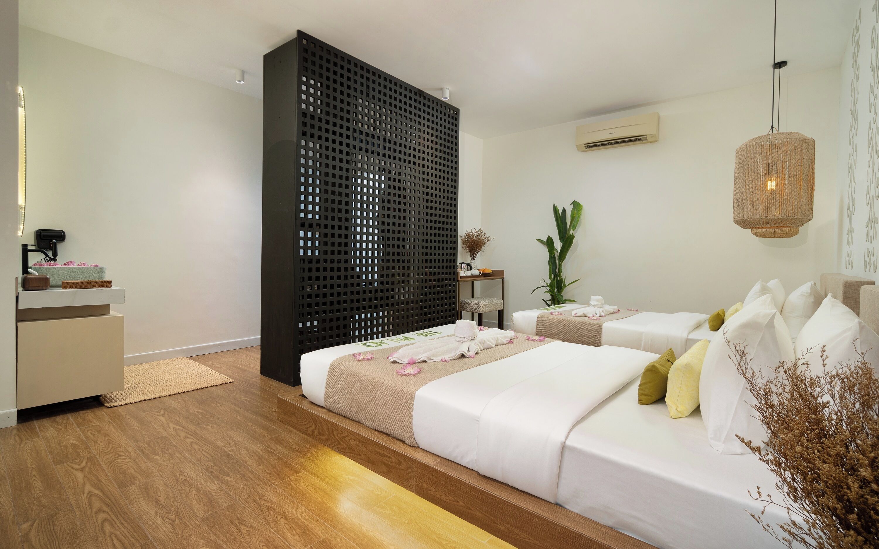 Un dormitorio moderno con suelo de madera, una cama grande, una mesita de noche pequeña, un aire acondicionado de pared y una lámpara colgante.