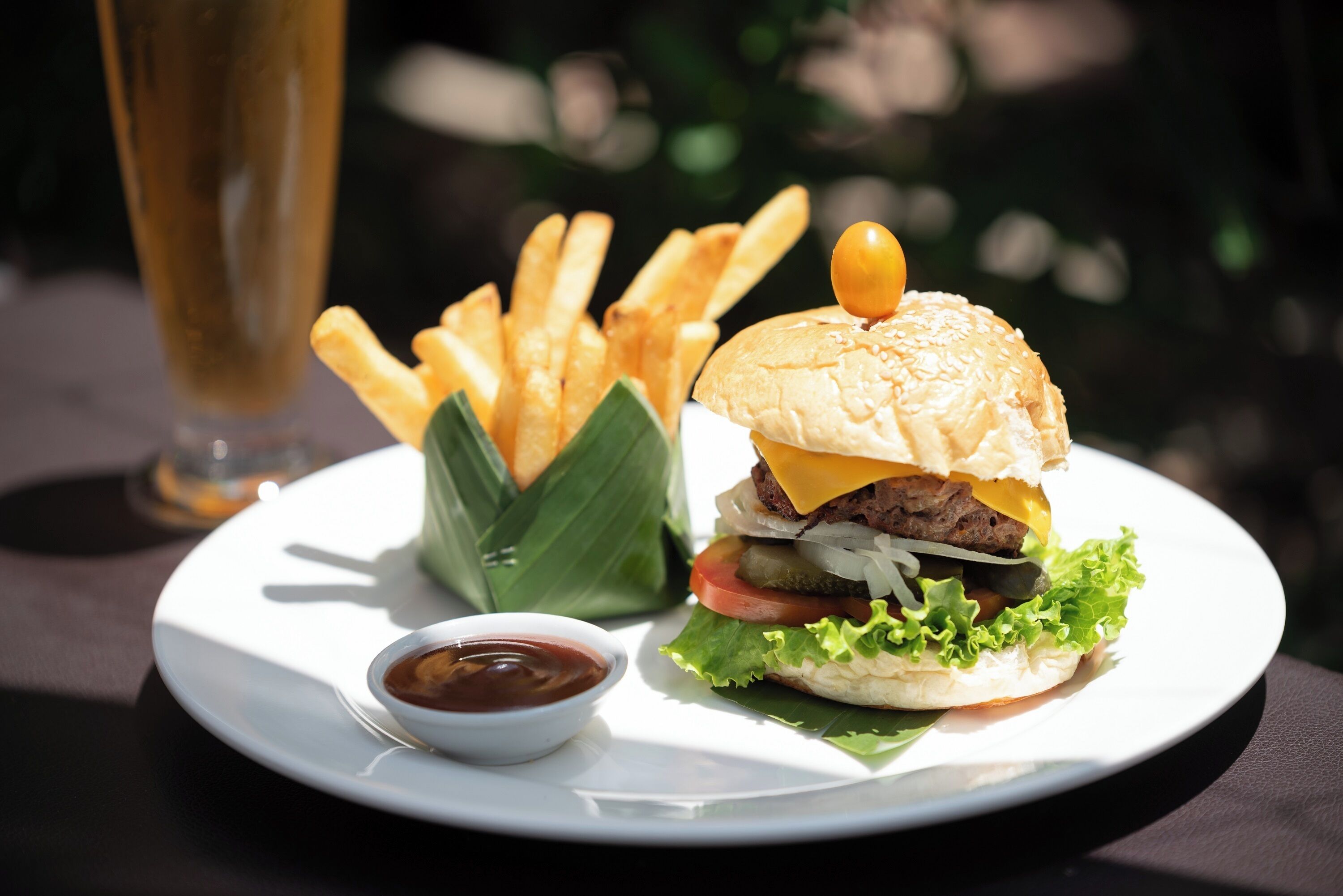A plate with a burger, fries, and a small bowl of sauce.