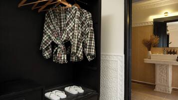 A bathroom with a black wall, a wooden hanger rack, a pair of white flip-flops, and a sink with toiletries.