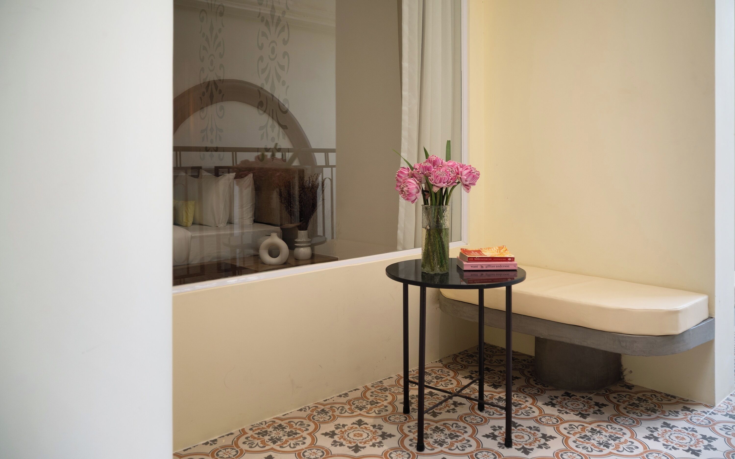 A small, elegantly decorated room with a bench, a table with a vase of flowers, and a window with a view of a balcony.