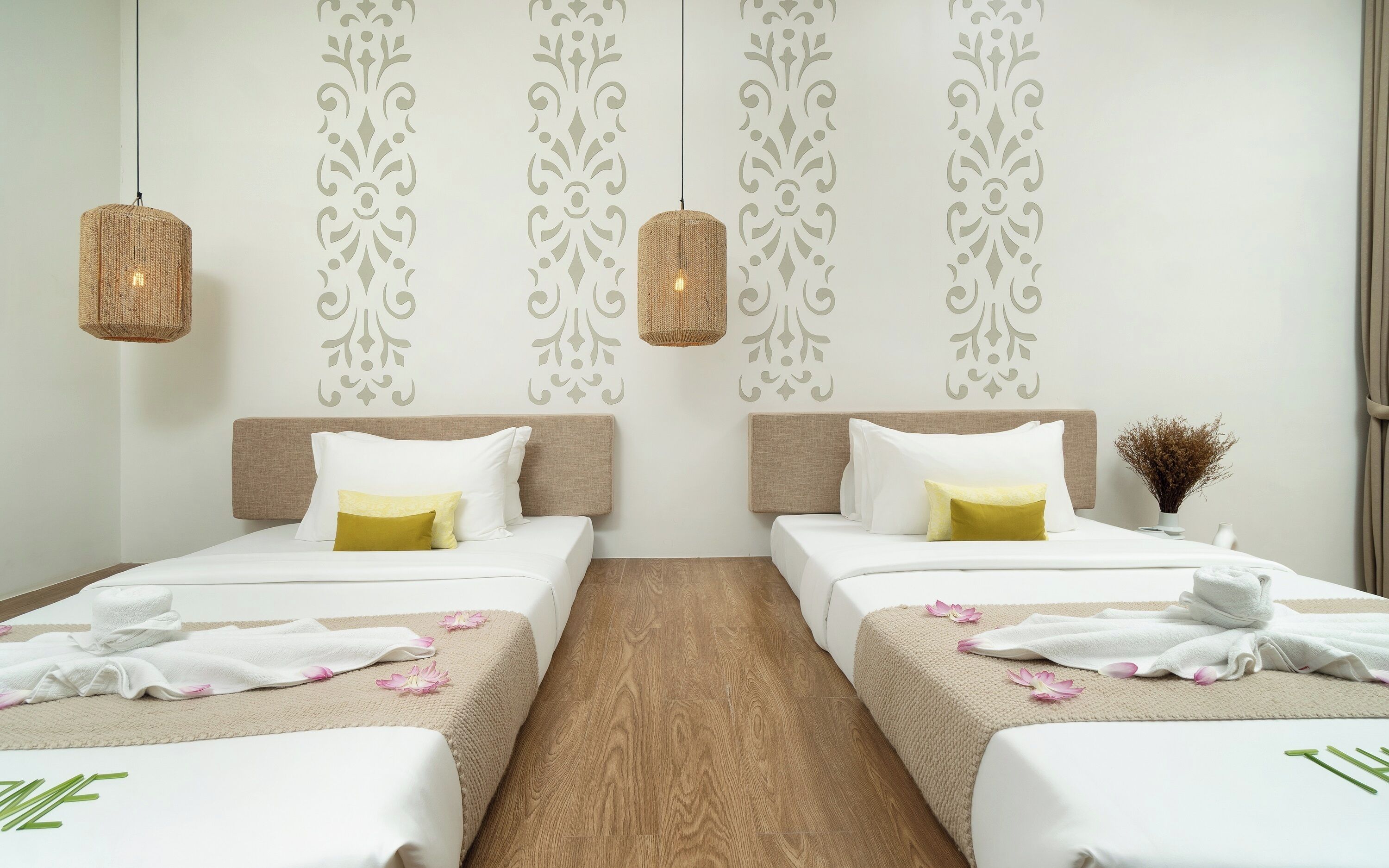A hotel room with two beds, a wooden floor, decorative wall patterns, and hanging wicker lamps.