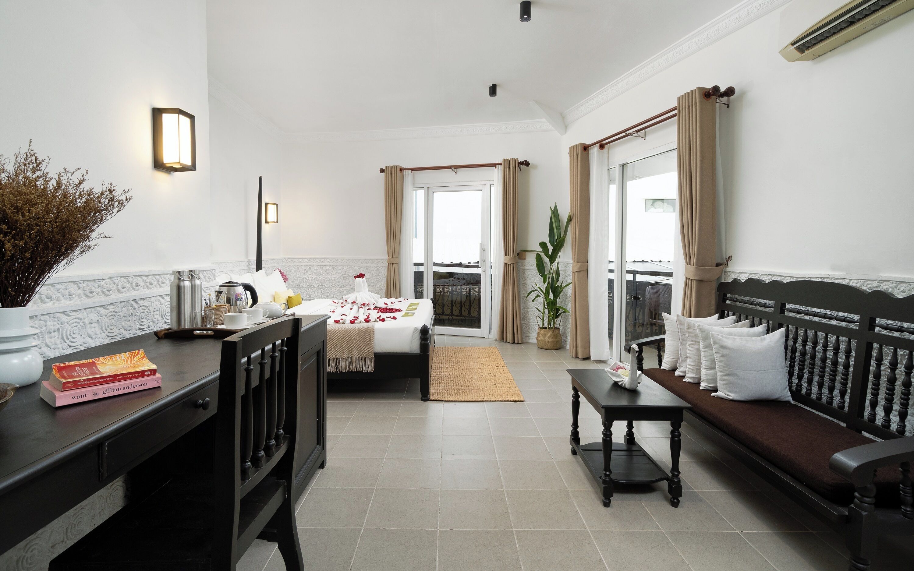 Habitación de hotel moderna con cama, sofá, mesa de comedor, cafetera y planta en maceta.
