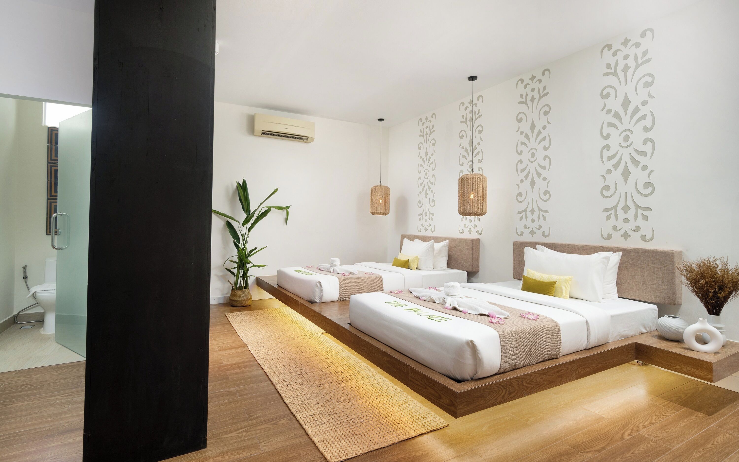 A modern hotel room with a large bed, bedside tables, a potted plant, and a bathroom visible through an open door.