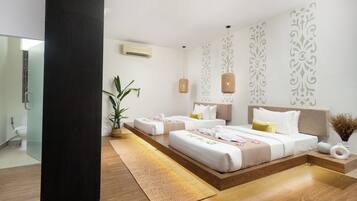 Une chambre d’hôtel moderne, dotée d’un grand lit, de tables de chevet, d’une plante en pot et d’une salle de bain visible à travers une porte ouverte.