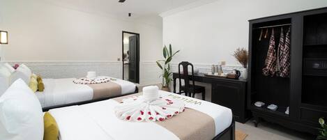 A hotel room with two beds, a desk, a wardrobe, a ceiling fan, and a potted plant.