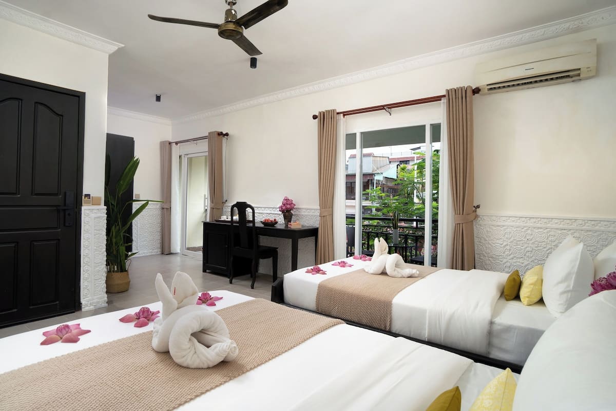 Habitación de hotel con dos camas, un escritorio, un ventilador de techo y vistas al exterior.