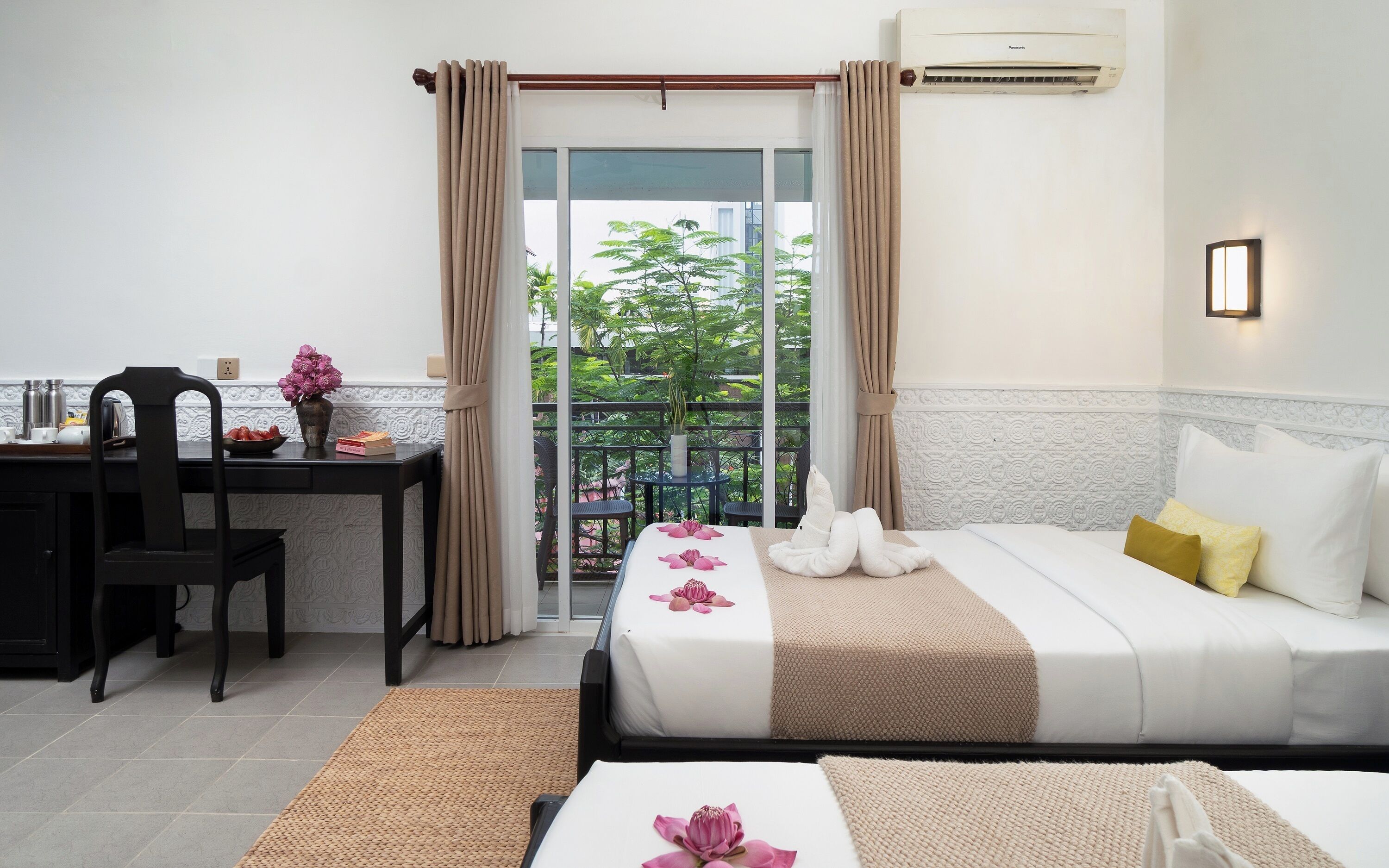 A hotel room with a bed, a desk, a chair, a balcony with a view, and an air conditioning unit.