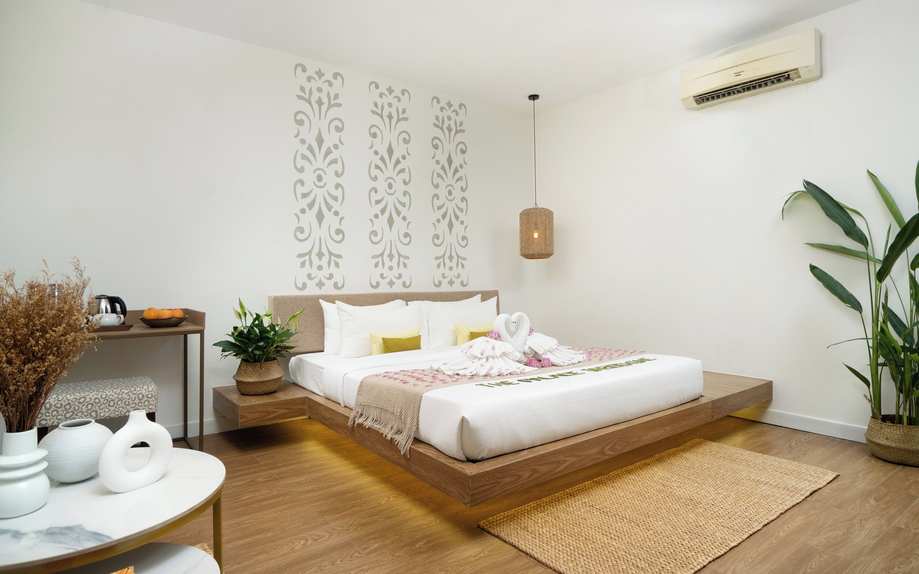 A modern bedroom with a bed, bedside table, potted plants, and a hanging light fixture.
