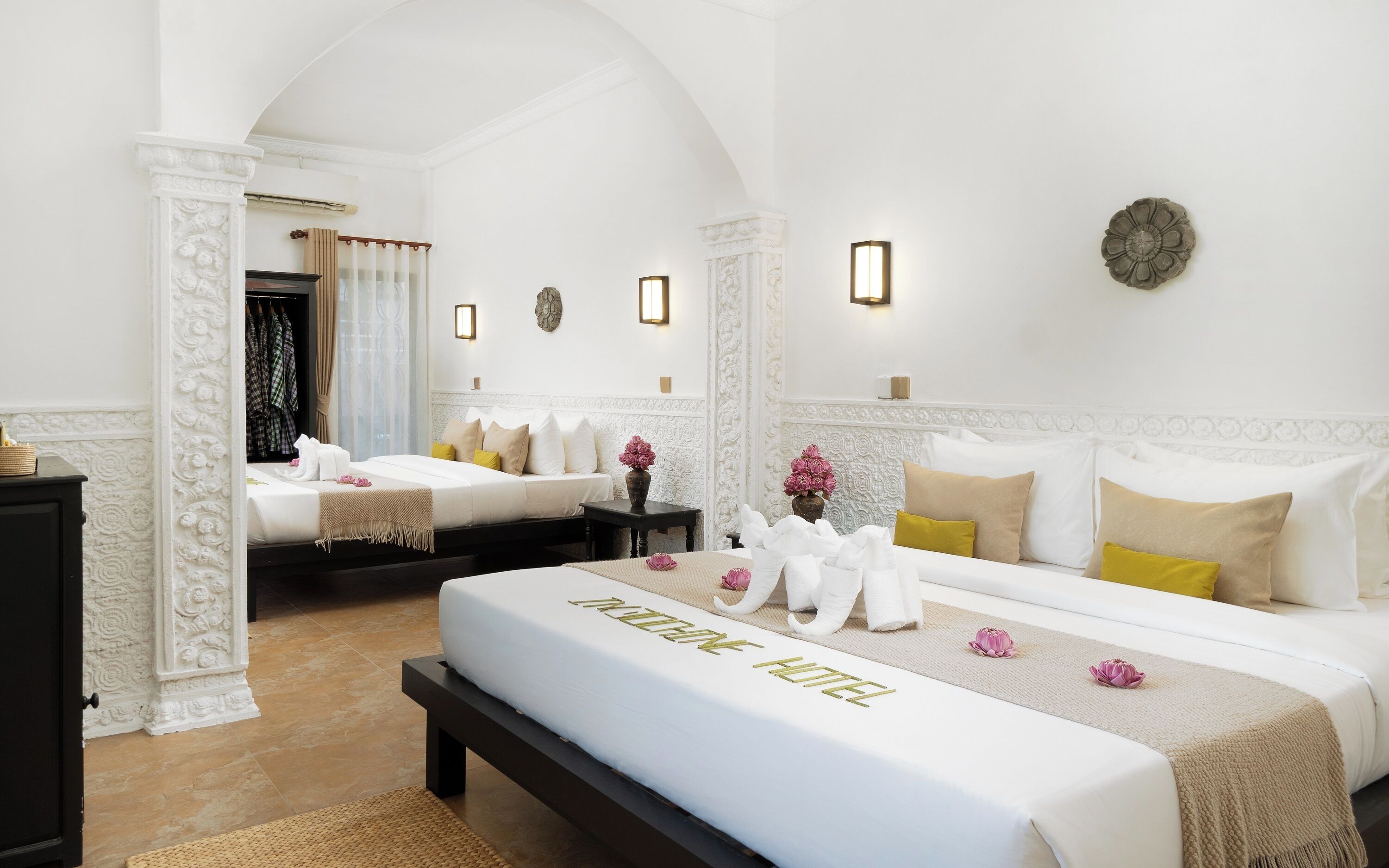 Habitación de hotel con dos camas, un banco, un espejo y un adorno en la pared.