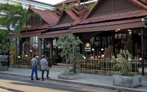 En traditionell byggnad med ett tak täckt av tegelpannor, en skylt med texten ”The Palace Indochine” och en grind som leder in till en entré prydd med krukväxter.