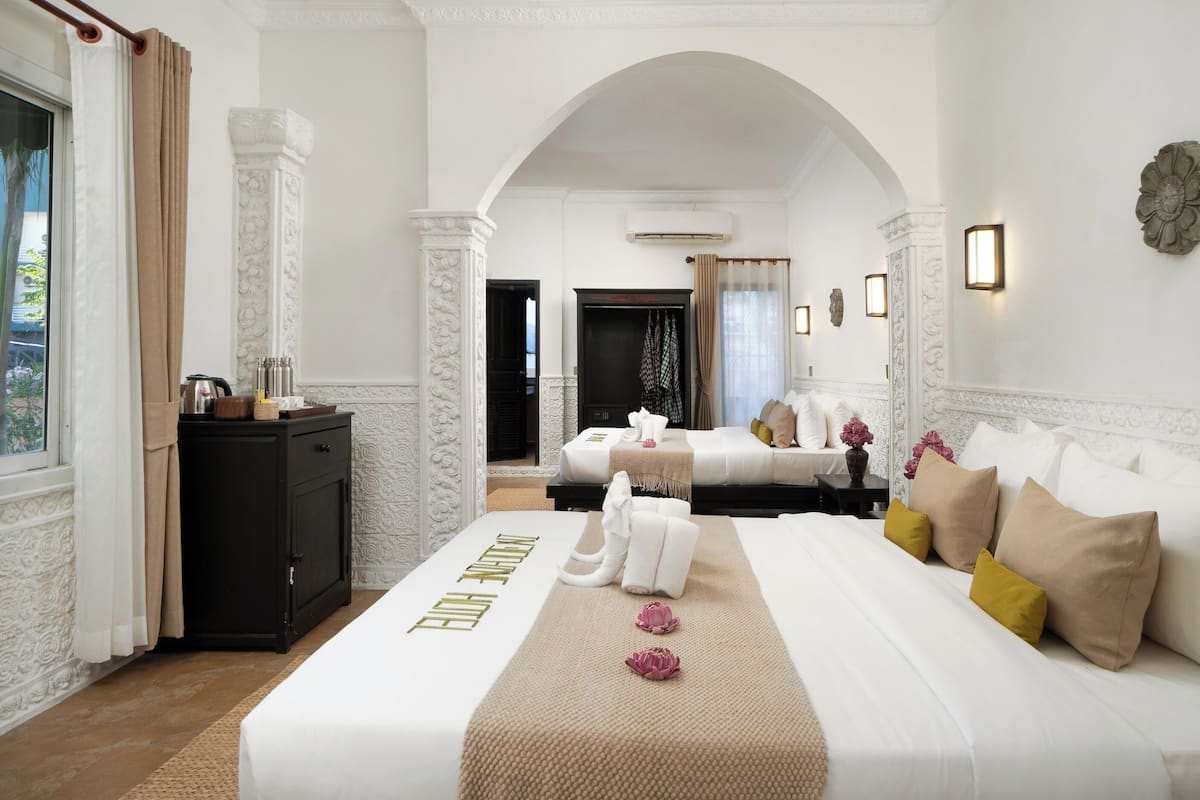 Habitación de hotel con cama, escritorio, armario y un arco que da a otra habitación.
