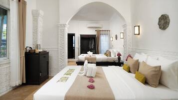 Une chambre d’hôtel comprenant un lit, un bureau, une armoire et une porte en arc donnant sur une autre pièce.