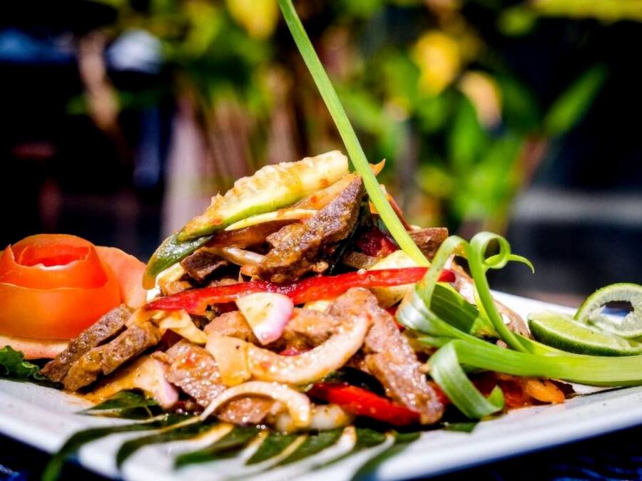 A plate of stir-fried meat with vegetables and a slice of lime.