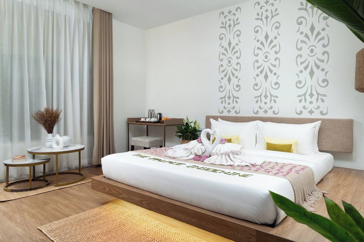 Una habitación de hotel con una cama grande, mesitas de noche y una pequeña mesa redonda con un florero y libros.
