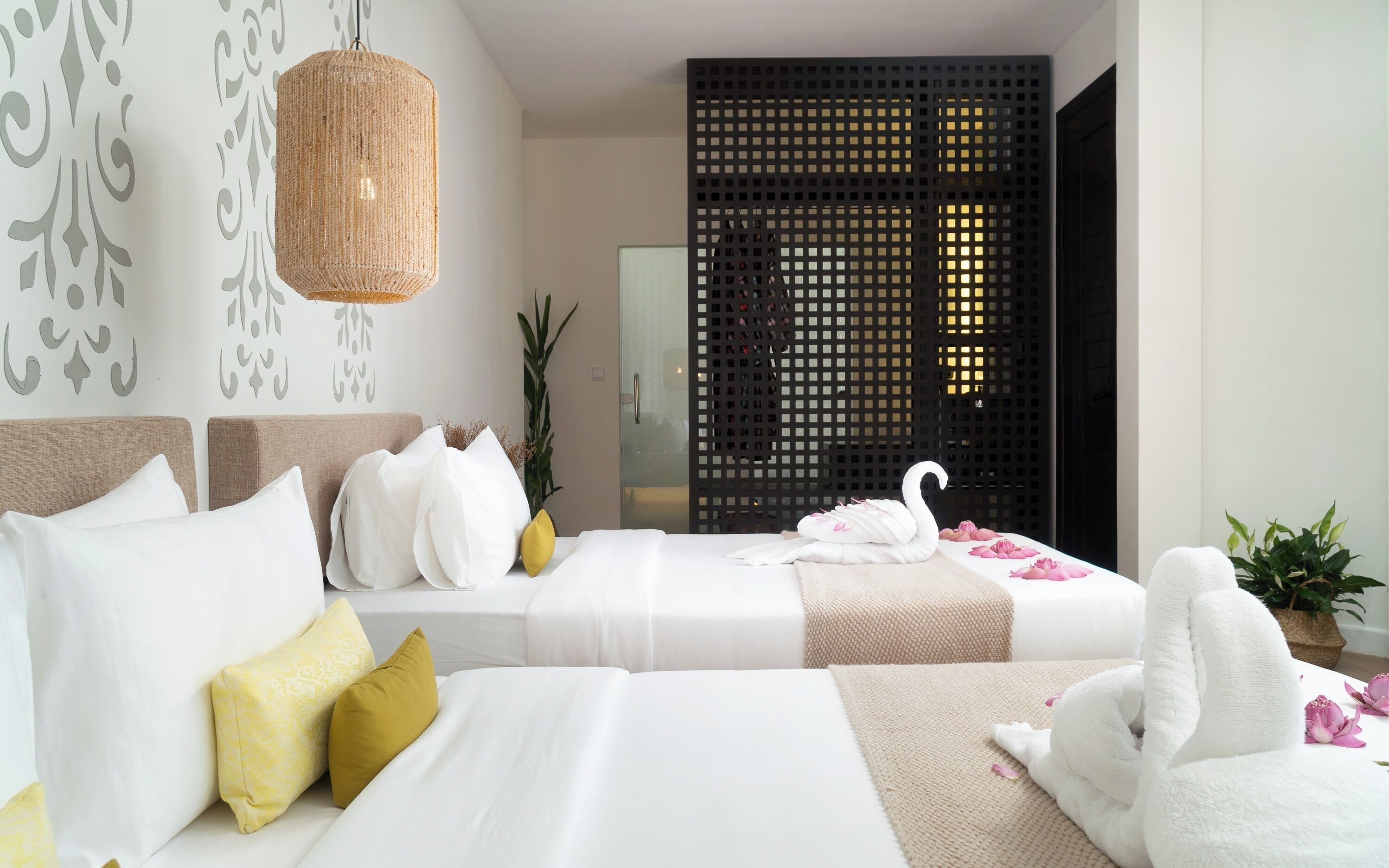 Une chambre d’hôtel avec deux lits, un luminaire en fibres tressées, un mur décoratif, une porte coulissante et une plante en pot.