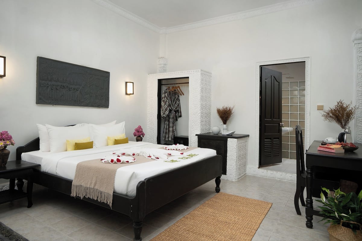 Un dormitorio con cama, mesitas de noche, cómoda, espejo y puerta que da a un baño.
