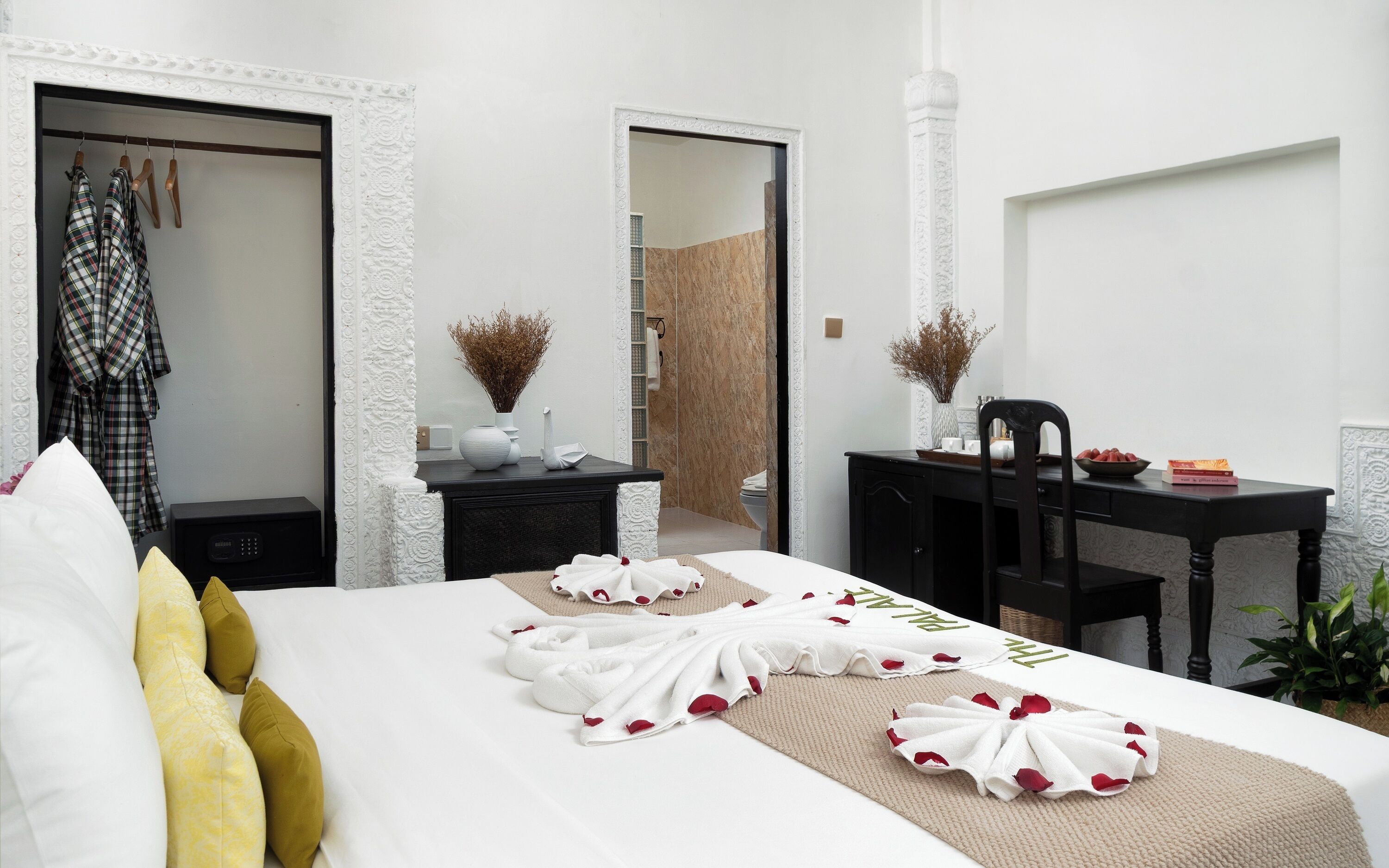 Habitación de hotel con cama, escritorio, silla, armario y baño visible a través de una puerta abierta.