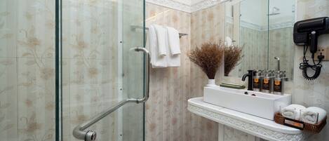 Et badeværelse med glasbrusekabine, hvid vask med toiletartikler og spejl med hårtørrer.