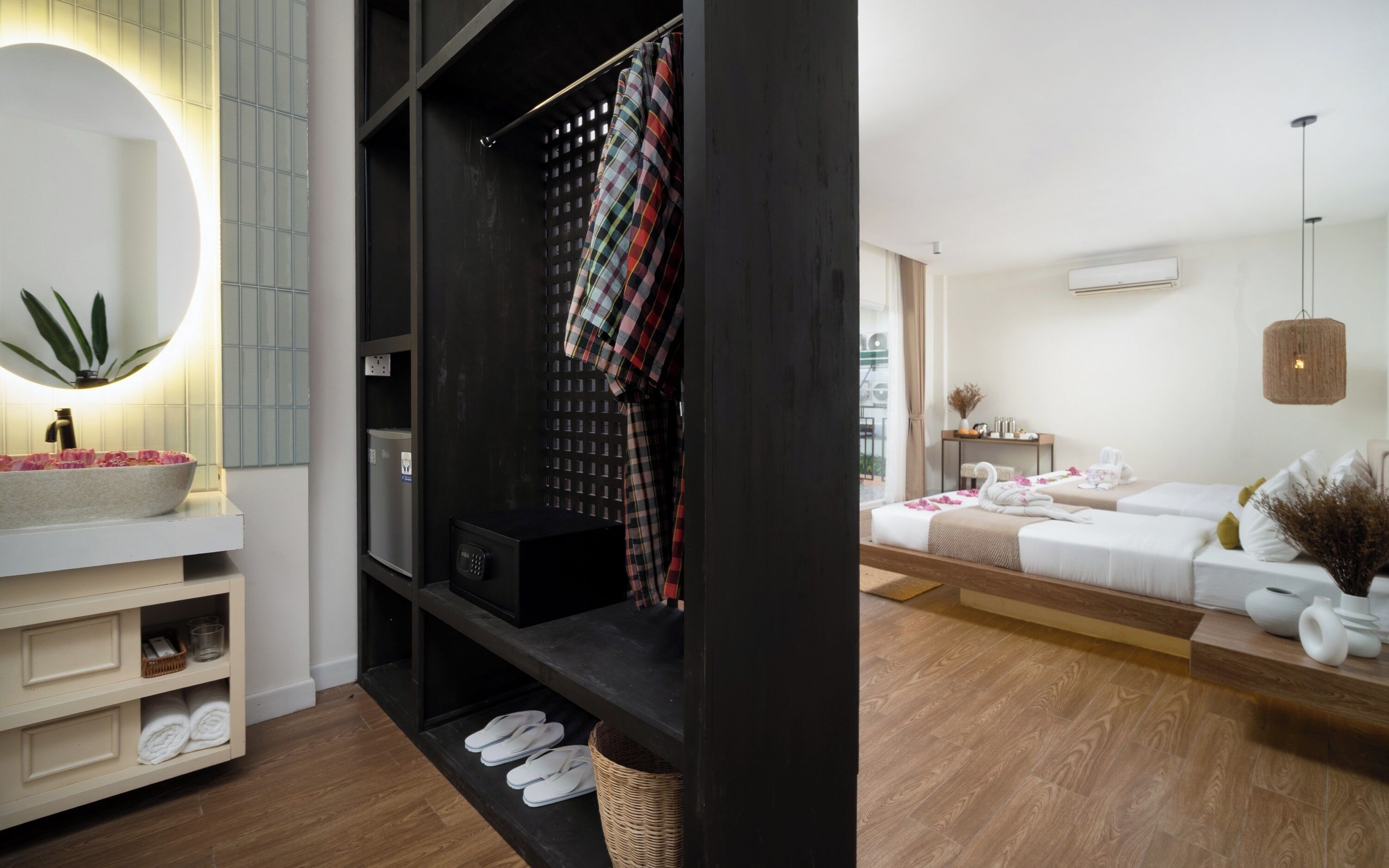 Une chambre d’hôtel moderne avec un grand miroir, un plancher en bois, une armoire noire, un canapé blanc et un luminaire suspendu.