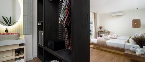 Une chambre d’hôtel moderne avec un grand miroir, un plancher en bois, une armoire noire, un canapé blanc et un luminaire suspendu.