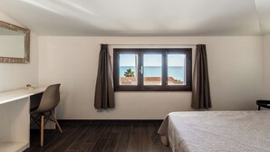 Una stanza con un letto, una scrivania, una sedia, una finestra con tende e vista sul mare.