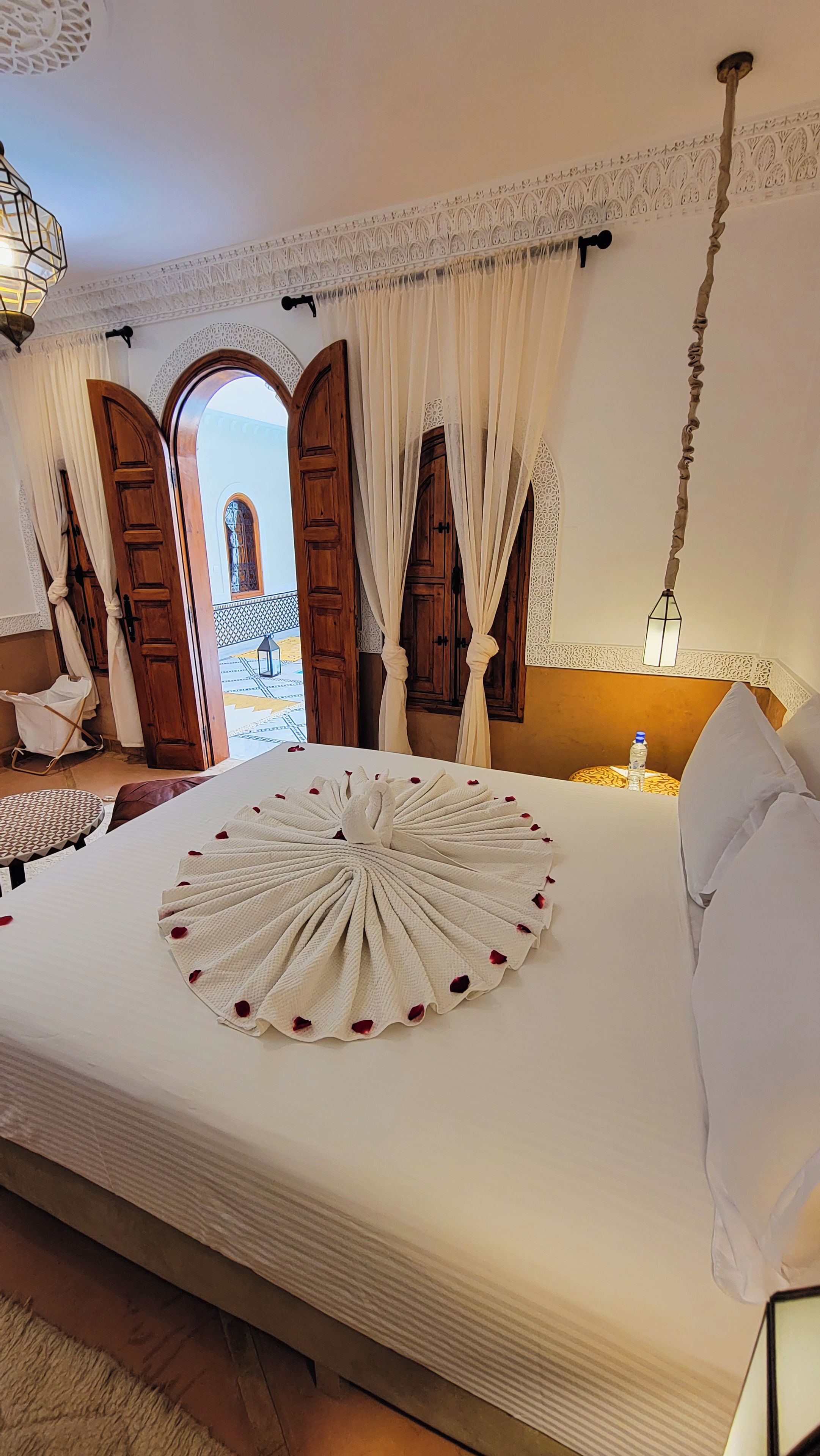 A hotel room with a large bed, a round decorative item on the bed, and a view of a courtyard through an open door.