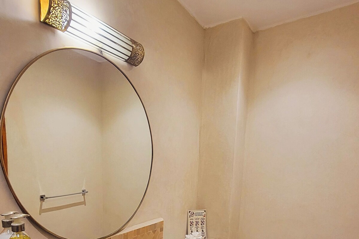 Un baño con un espejo grande, un lavamanos, un inodoro y un cubo de basura.