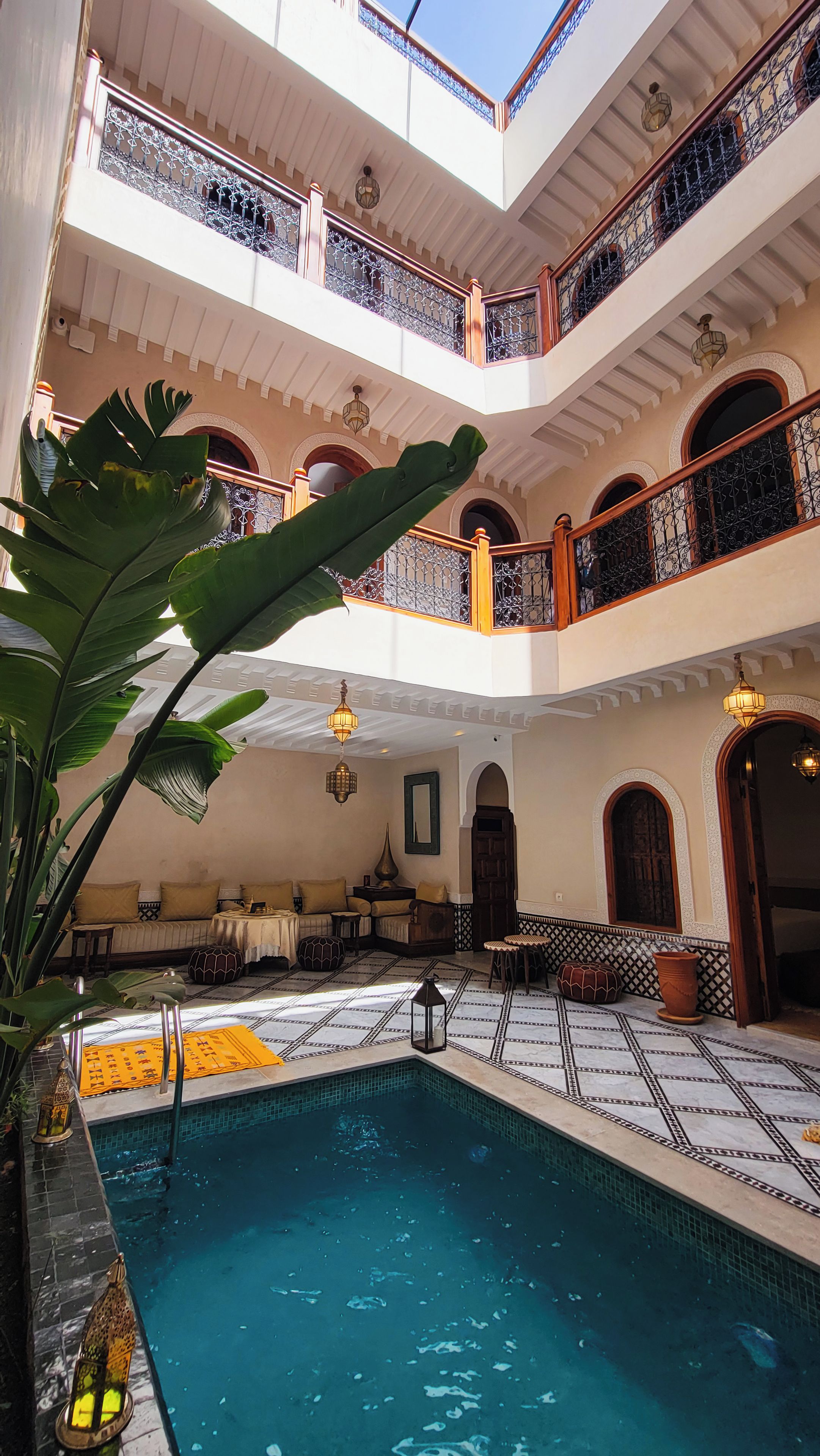 A multi-level indoor swimming pool with a tiled floor, surrounded by seating areas and a balcony with ornate railings.