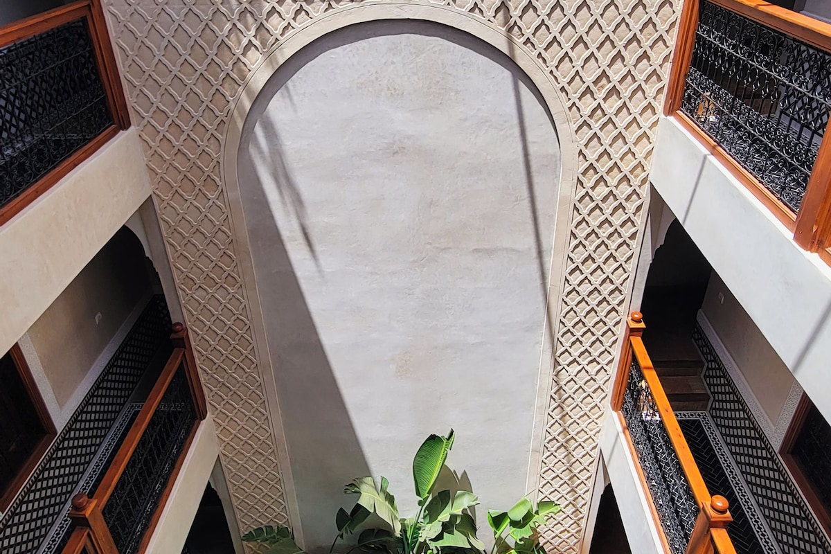 Un área de piscina con un muro de diseño geométrico, un arco central y suelo de baldosas.