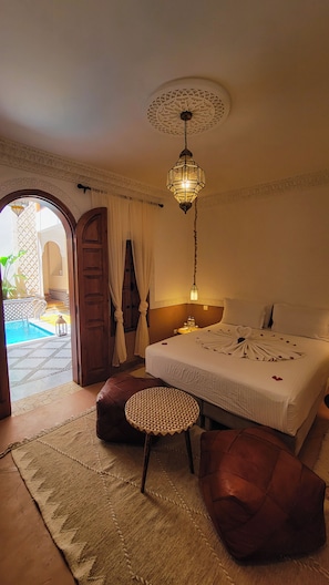 A hotel room with a bed, a round table, a hanging light fixture, and a view of an outdoor swimming pool. - Maison Kays  (Marrakech)