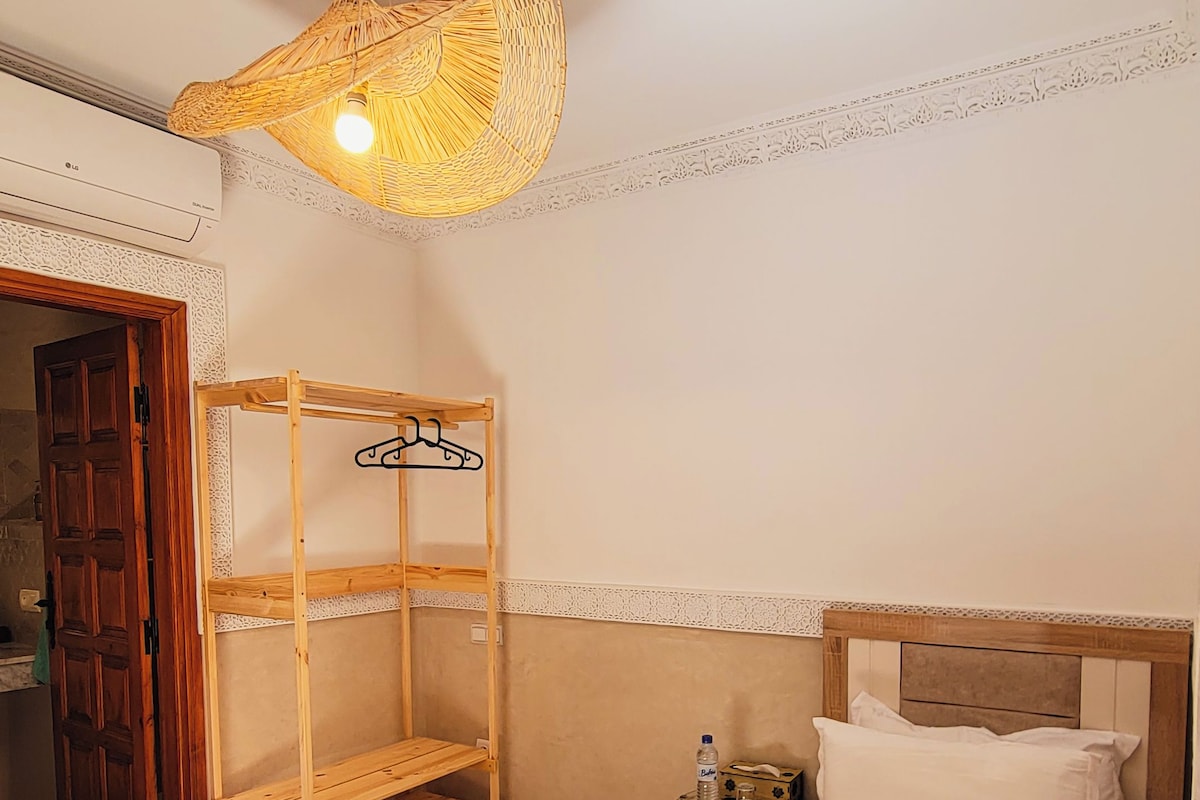 Habitación de hotel con una cama, una estantería de madera, una lámpara colgante y una puerta.
