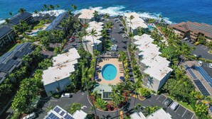 Vista aérea de um resort com piscina central, rodeado por palmeiras e edifícios com painéis solares.