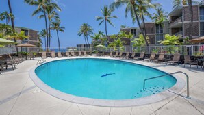 Uma piscina cercada por espreguiçadeiras e palmeiras, com um edifício ao fundo.