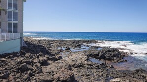 Uma costa rochosa com um edifício com grandes janelas e varanda.