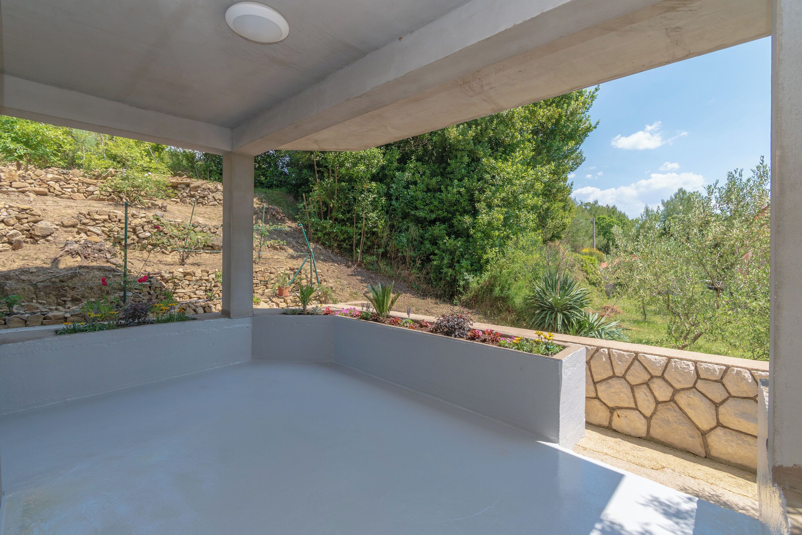 A covered outdoor area with a stone wall and greenery.