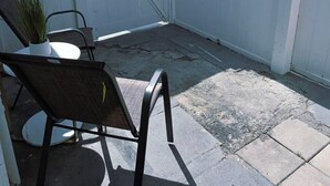 A covered patio area with a white fence, a potted plant, and a metal chair.