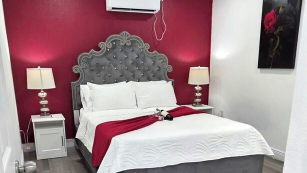 A bedroom with a bed, nightstands, an air conditioning unit, and a painting on the wall.