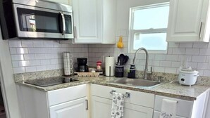 A kitchen with white cabinets, a microwave, a sink, and a window.