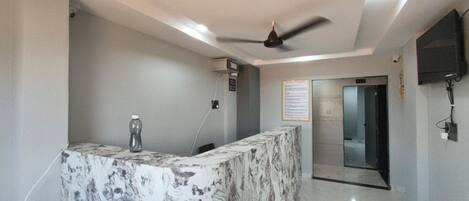 A reception area with a marble counter, ceiling fan, and a glass door leading to an elevator.