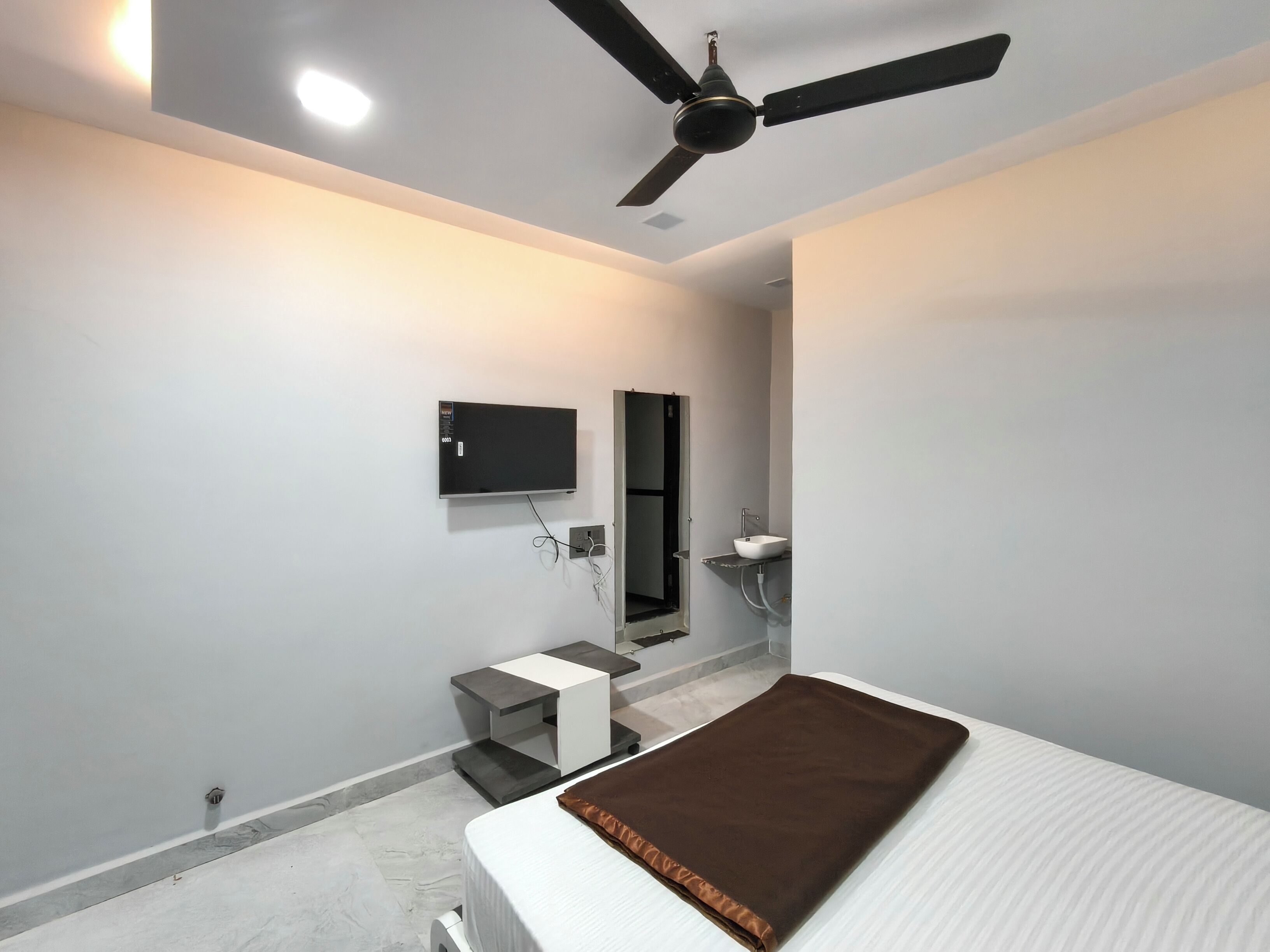 A bedroom with a bed, a ceiling fan, a TV, a mirror, and a small bedside table.