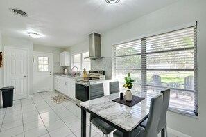 Cocina moderna con armarios blancos, campana extractora de acero inoxidable y un comedor con mesa y sillas de mármol.