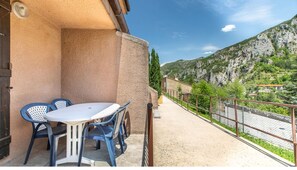 A balcony with a table and chairs, a view of a mountain, and a fence.