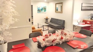 Ein Essbereich mit einem Tisch für vier Personen, einem grauen Sofa, einer modernen Pendelleuchte und einem Wandbild.